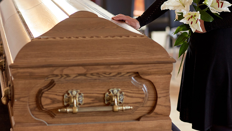 John Wilde Coffin Handle & Funeral Furnishing Supplier Woman puts hand on coffin at funeral.